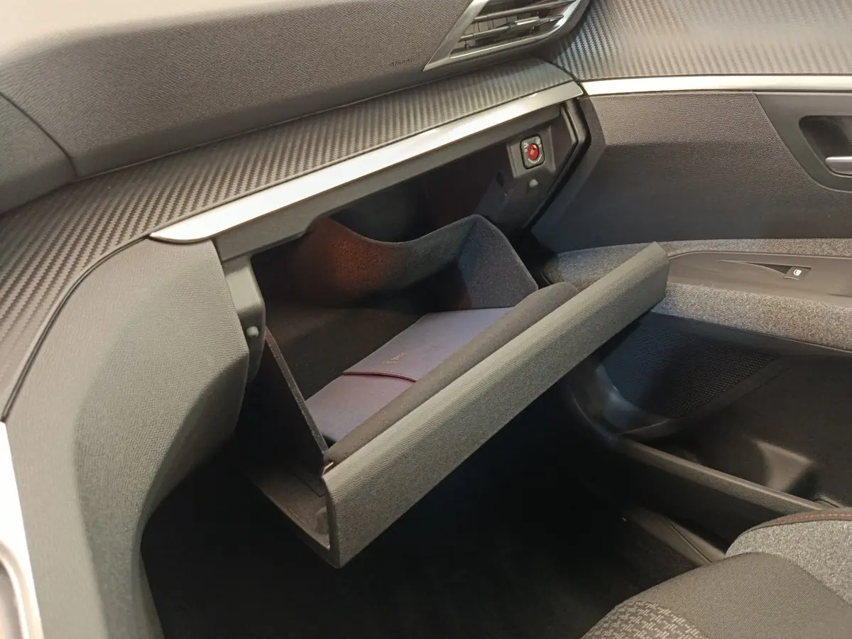 Gros plan sur la boîte à gants ouverte côté passager du Peugeot 3008 gris foncé, montrant un livret à l'intérieur.