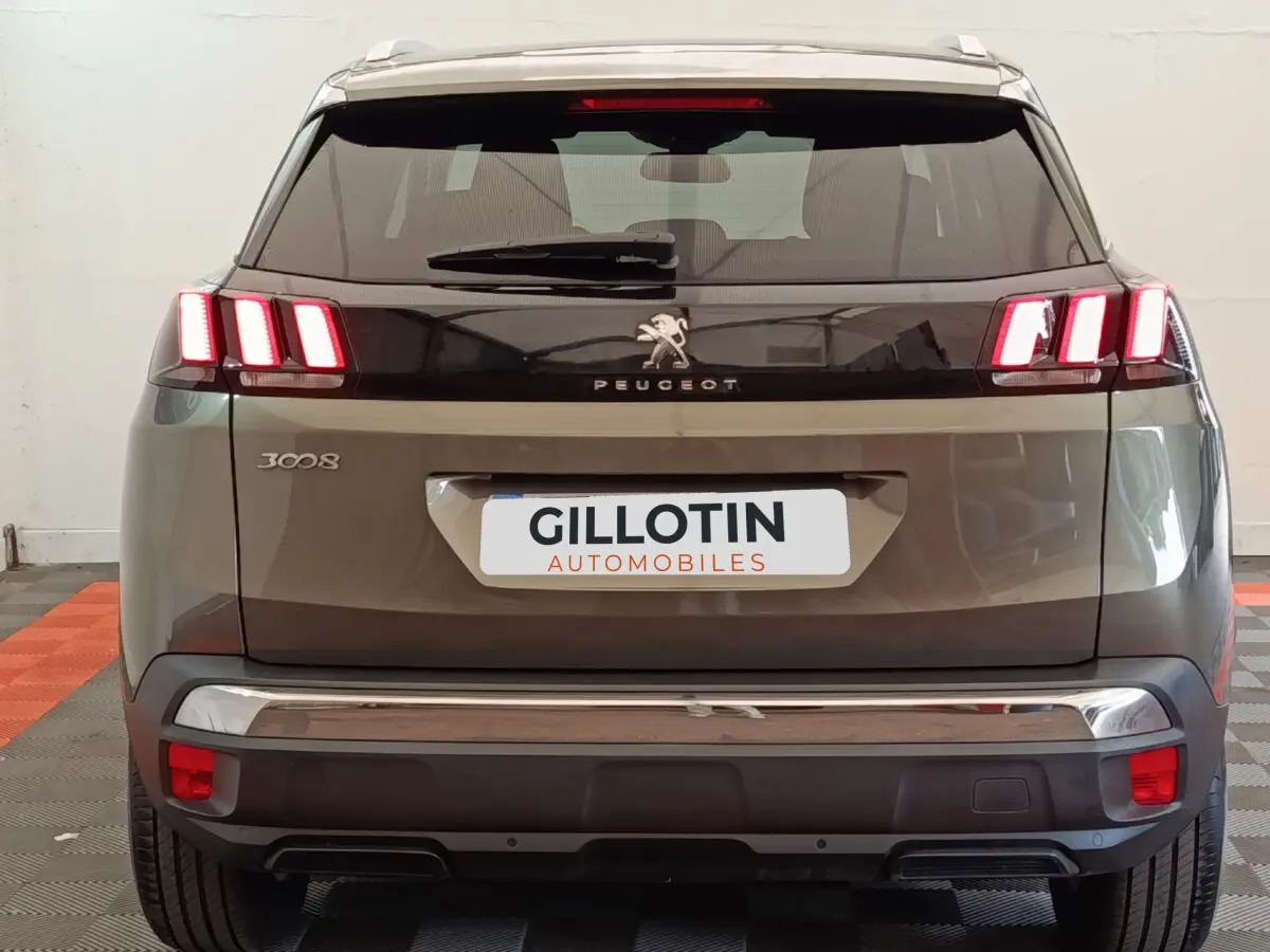 Vue arrière d'un Peugeot 3008 gris foncé avec feux arrière LED caractéristiques allumés et logo central visible.