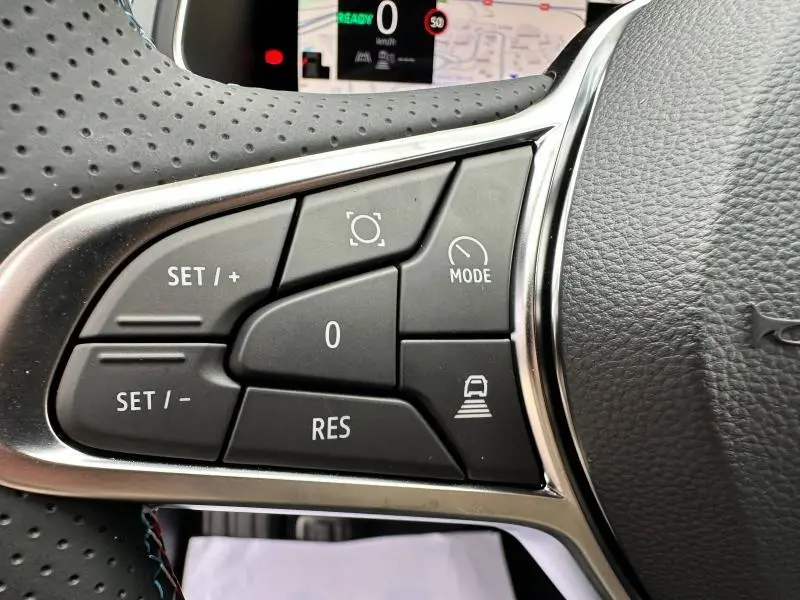 Gros plan sur les commandes du volant du Renault Captur 1.6 E-Tech hybride 2025, finition esprit Alpine avec surpiqûres bleues.