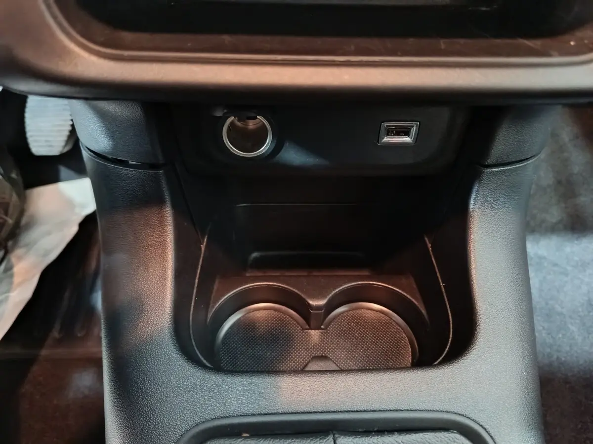 Gros plan sur la console centrale noire de la Citroën C3 2024, montrant porte-gobelets, prise 12V et port USB.