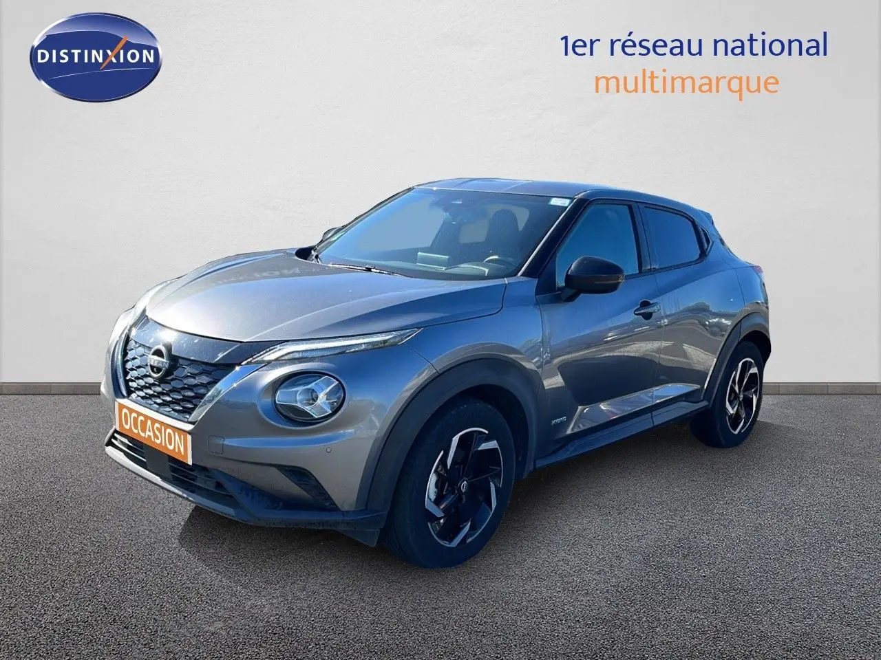 Nissan Juke Hybrid gris squale metal en 3/4 avant droit, avec jantes noires et détails noirs contrastants.