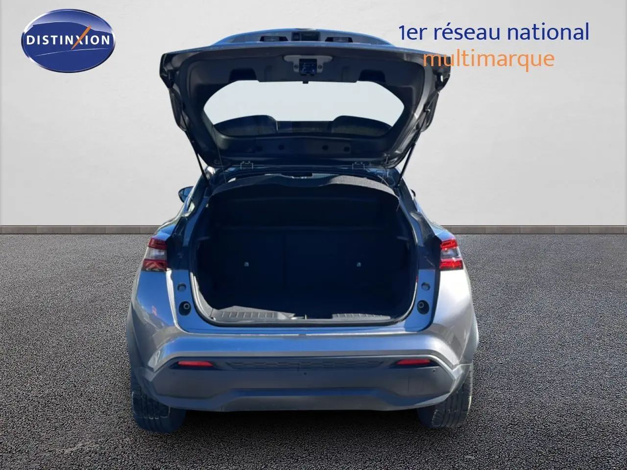 Vue arrière d'un Nissan Juke Hybrid gris squale métal 2024 avec coffre ouvert sur fond neutre.