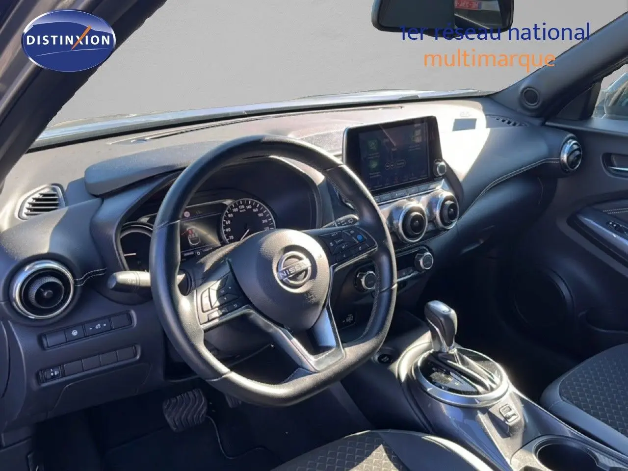 Vue intérieure du poste de conduite du Nissan Juke Hybrid 2024, avec volant multifonction et console centrale grise métallique.