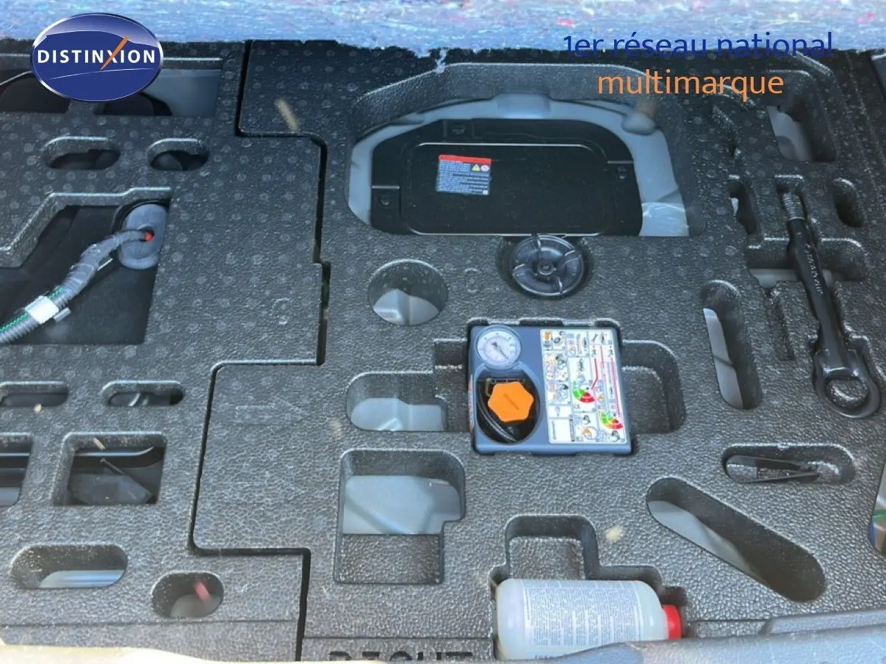 Vue en plongée sur le coffre ouvert du Nissan Juke gris squale métal, montrant le rangement et kit de réparation pneus.