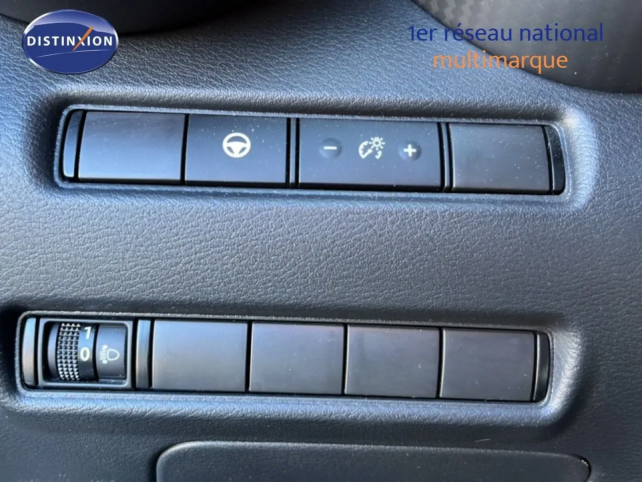 Gros plan sur les commandes de réglage de luminosité et assistance au volant du tableau de bord d’un Nissan Juke gris squale métal.
