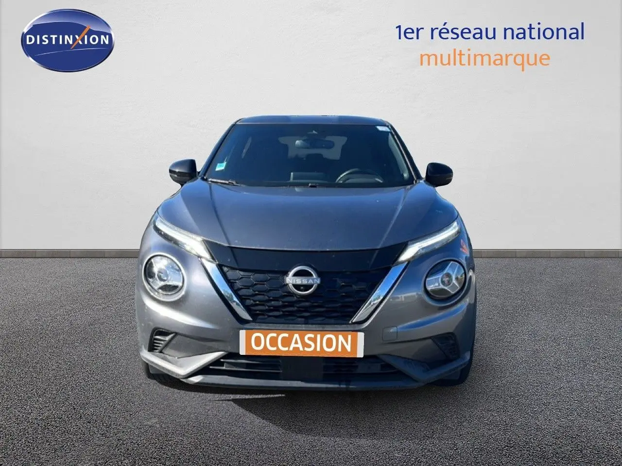 Vue avant d'un Nissan Juke Hybrid gris squale métal avec calandre noire et phares ronds distinctifs.