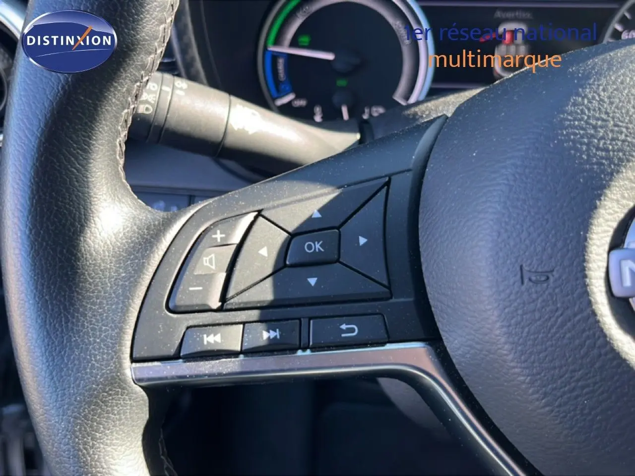 Gros plan sur les commandes au volant côté gauche du Nissan Juke 2024 gris squale métal, avec tableau de bord hybride en arrière-plan.
