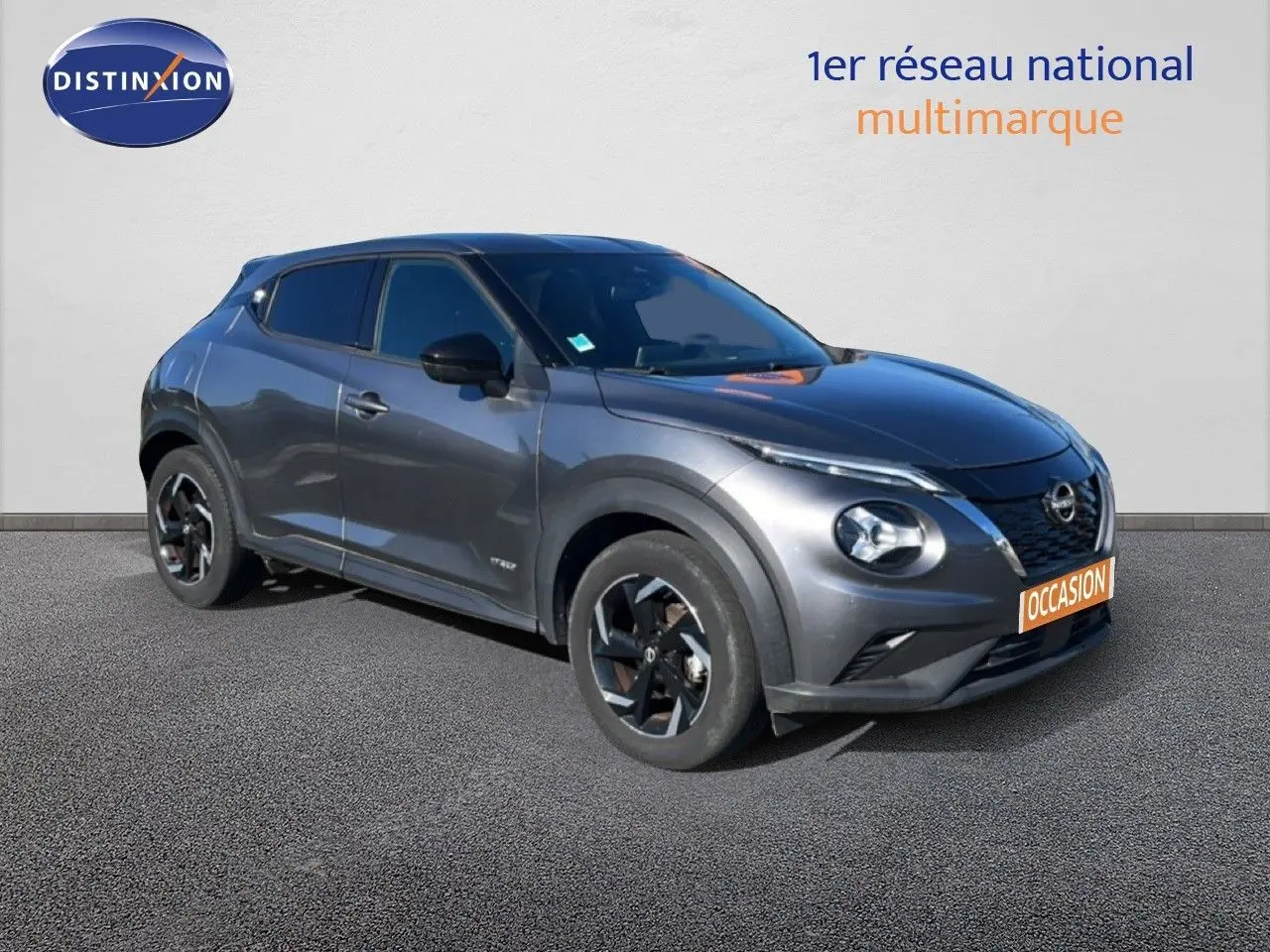 Nissan Juke Hybrid gris squale métal vu en 3/4 avant droit avec jantes noires et toit foncé.