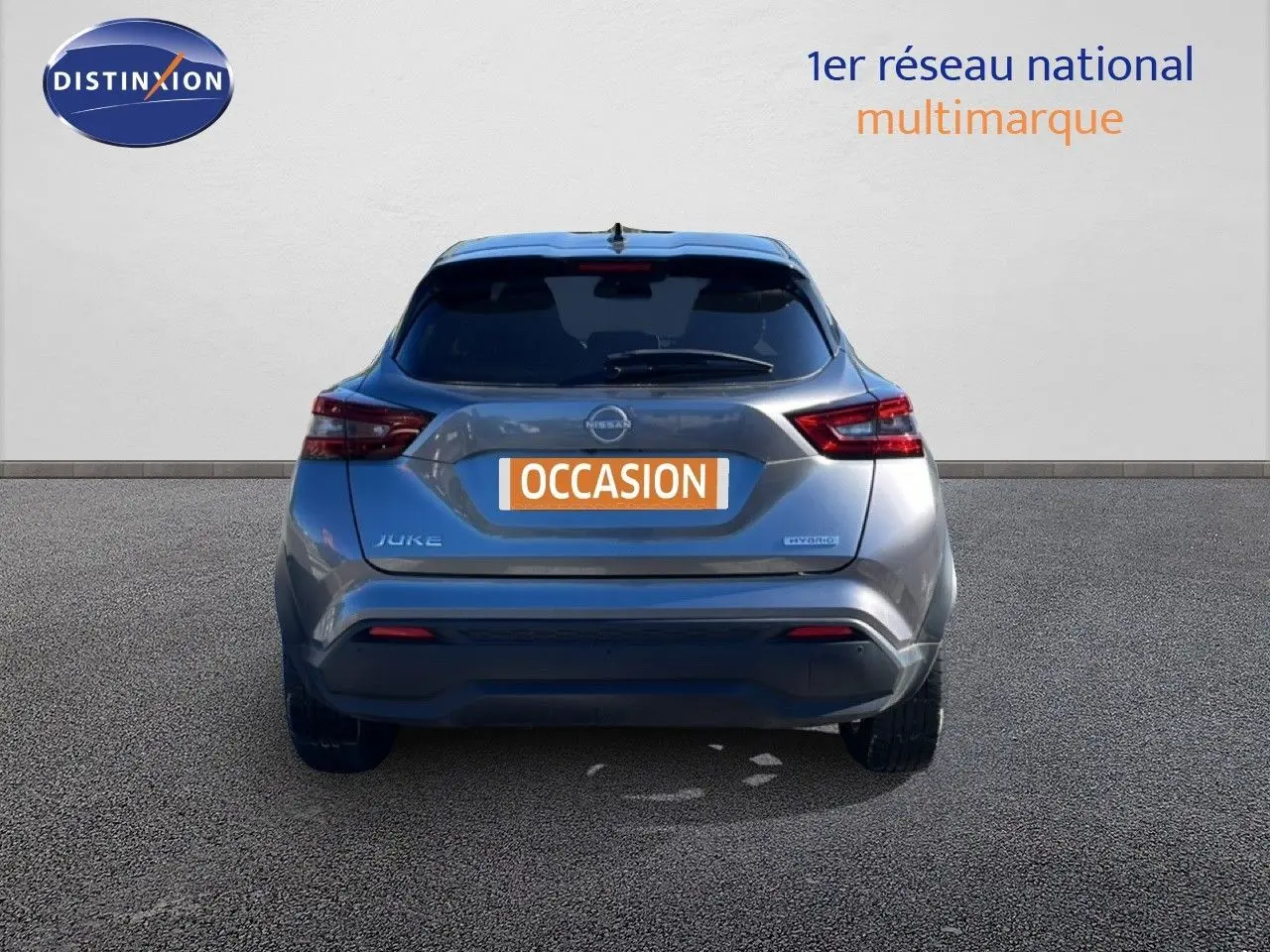 Vue arrière d’un Nissan Juke Hybrid gris squale métal avec plaque « OCCASION » sur fond neutre.