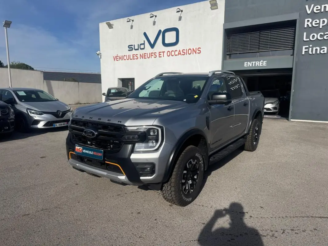 Ford Ranger Wildtrak gris vu en 3/4 avant droit, avec barres de toit et jantes alliage noires.