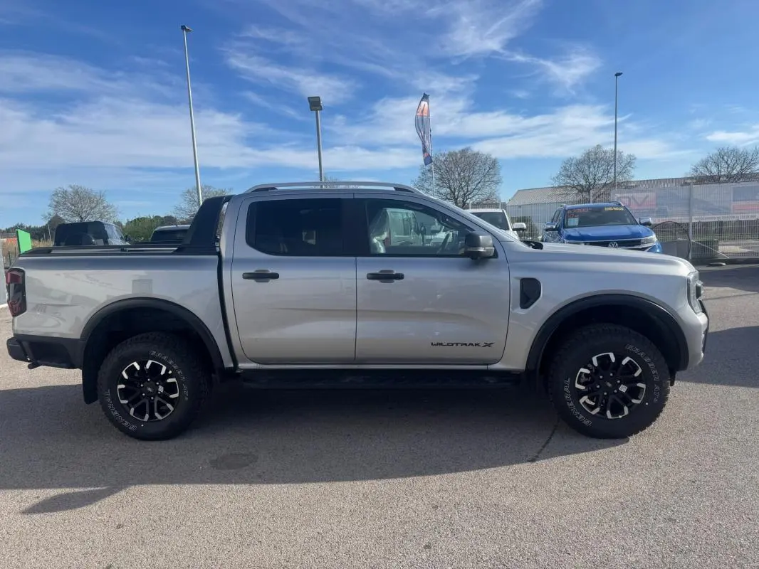 Vue de profil côté gauche du Ford Ranger gris 2025 Wildtrak X avec jantes alliage noires et barres de toit visibles.