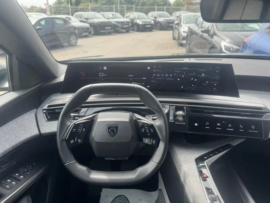 Vue intérieure centrée sur le volant Peugeot et le cockpit numérique large du 5008 noir, avec tableau de bord moderne et écran tactile.