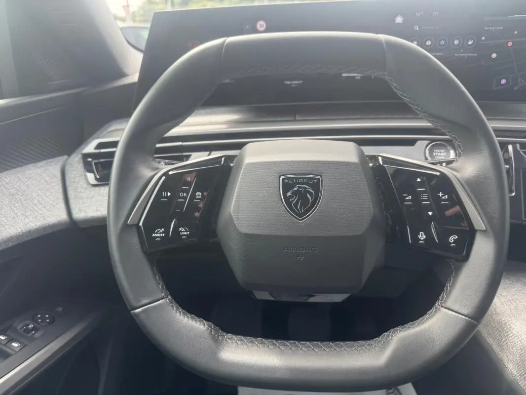 Gros plan sur le volant cuir noir du Peugeot 5008 2025 avec commandes intégrées et logo Peugeot central.