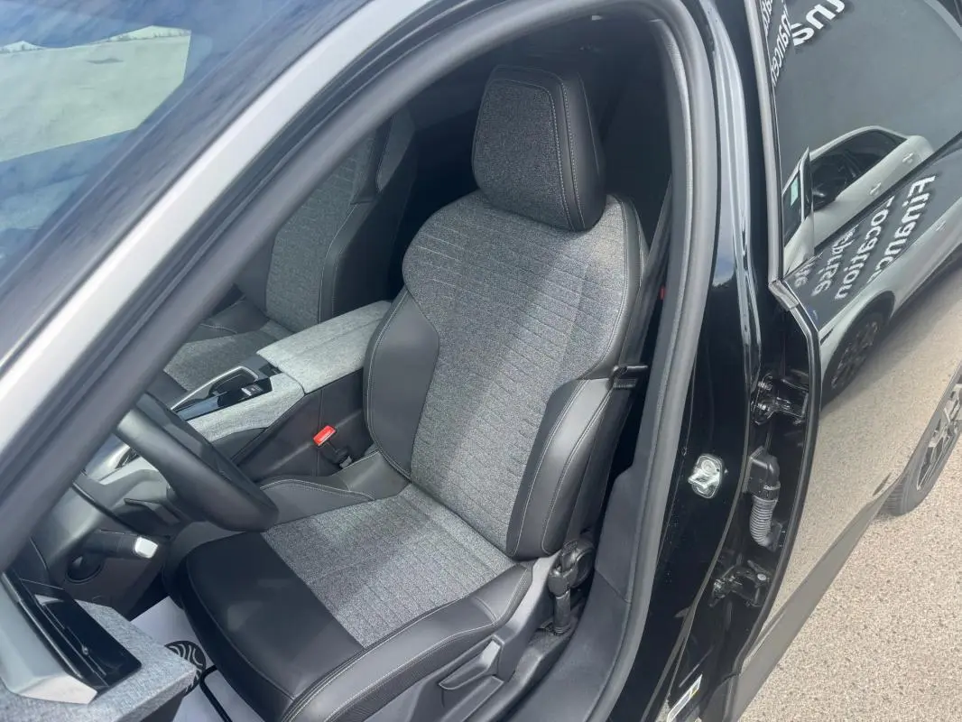 Vue intérieure côté conducteur du Peugeot 5008 noir 2025, mettant en valeur le siège tissu et cuir avec accoudoir central.