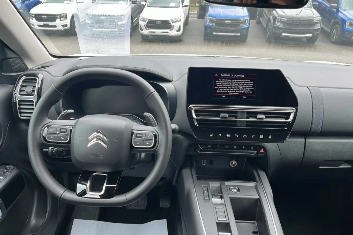 Vue intérieure avant du Citroën C5 Aircross blanc, volant cuir multifonctions et écran tactile central allumé.