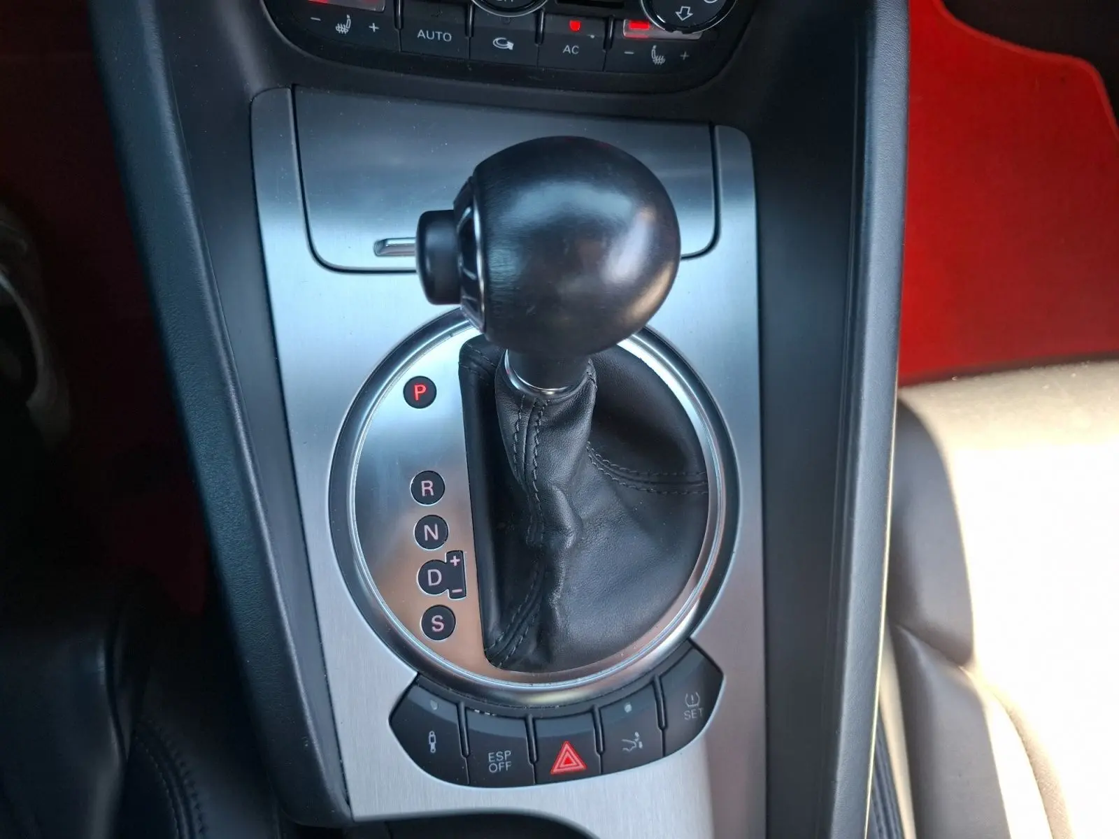 Gros plan sur la commande de boîte automatique d’une Audi TT rouge, avec levier en cuir et console alu brossé.