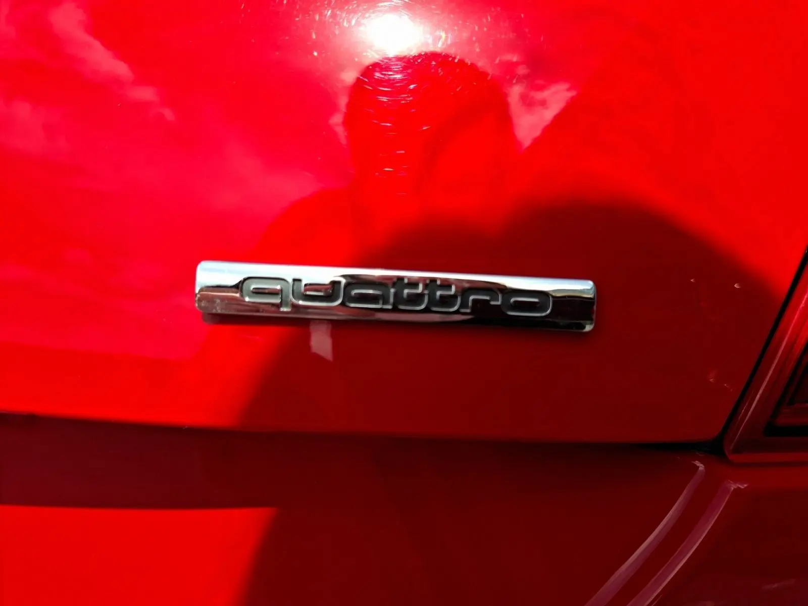 Gros plan sur l’inscription « quattro » chromée à l’arrière d’une Audi TT rouge vif, sous un angle latéral droit.