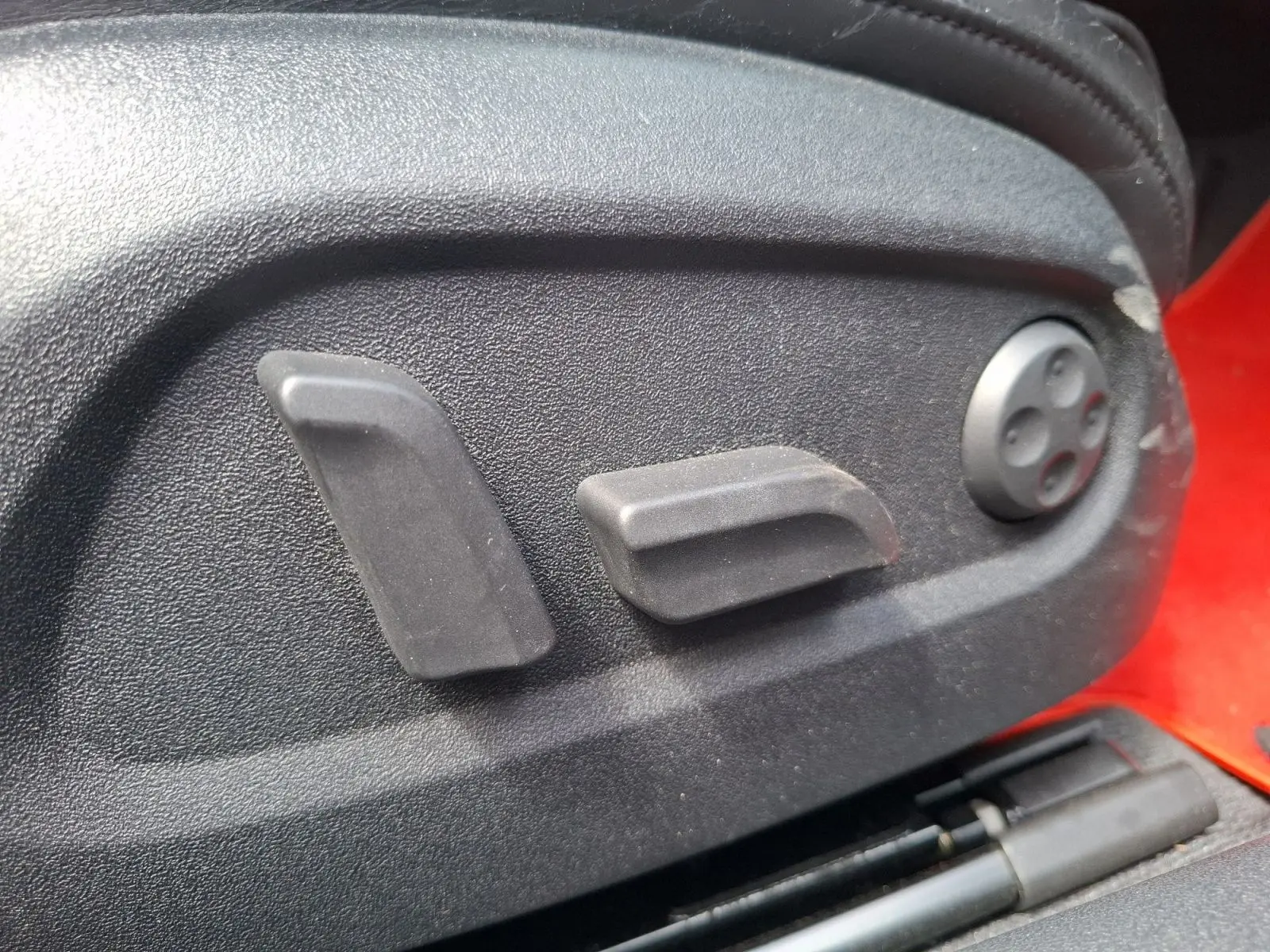 Détail des commandes de réglage électrique du siège côté conducteur d’un Audi TT rouge, vue rapprochée.