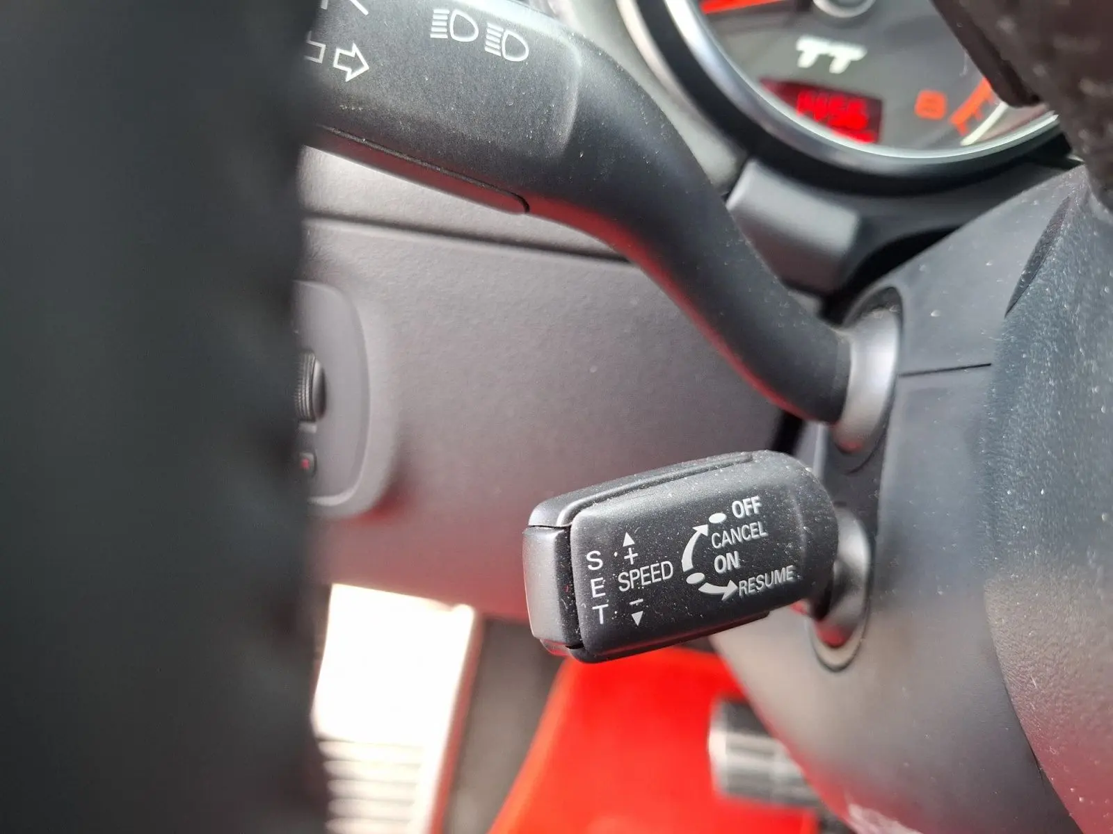 Gros plan sur le levier de régulateur de vitesse de l'Audi TT rouge, visible derrière le volant côté gauche.