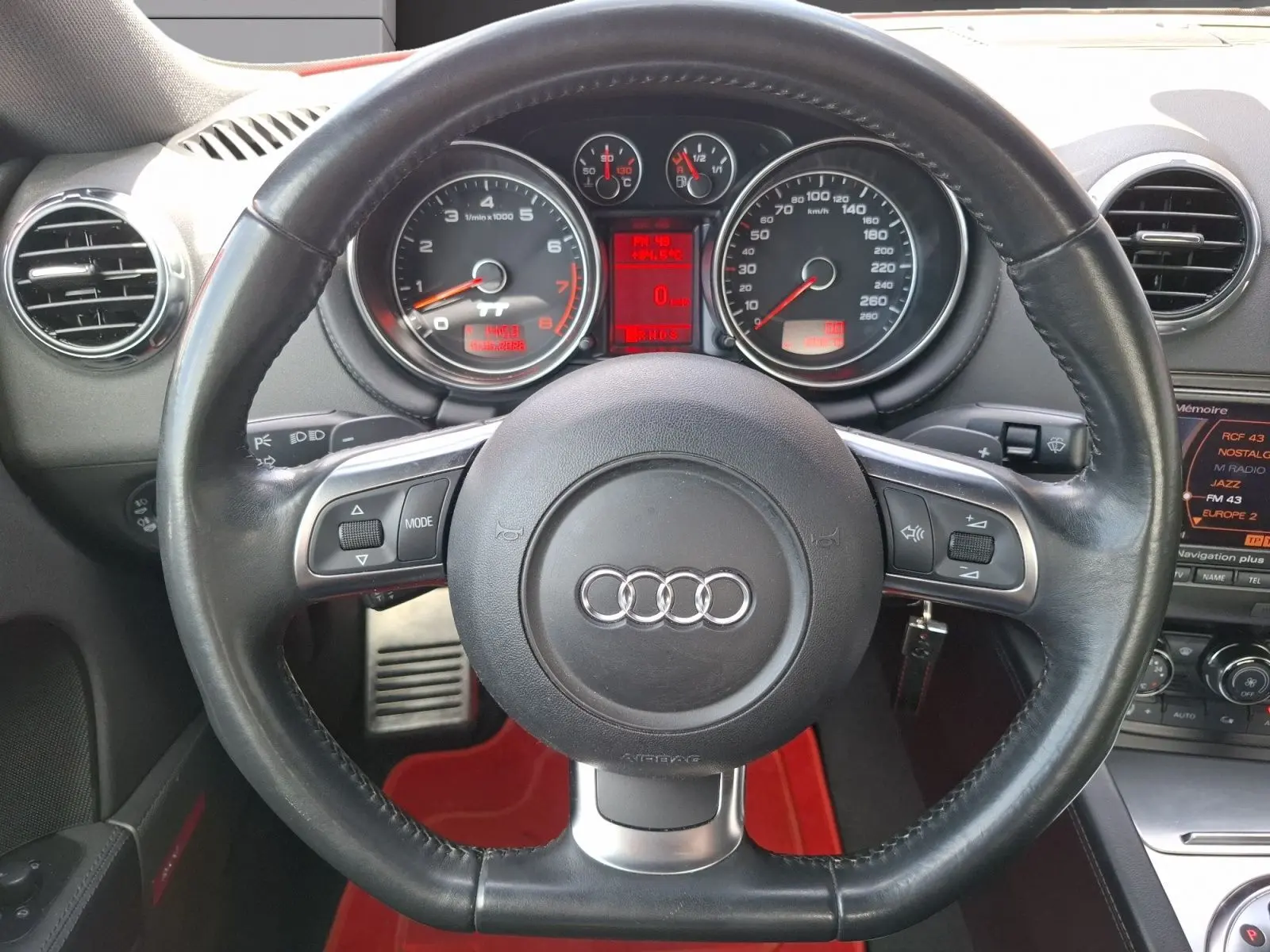 Vue centrée sur le volant en cuir noir d'une Audi TT 3.2 V6 Quattro 2007 avec palettes au volant et tableau de bord rouge.