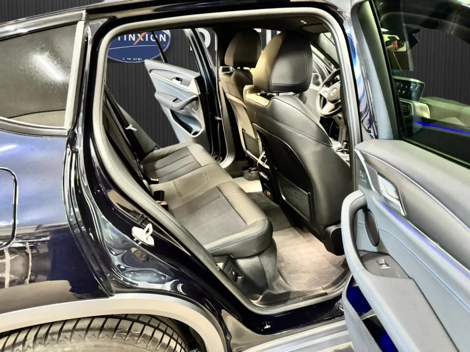 Vue intérieure côté gauche arrière d'un BMW X4 Carbonschwarz 2020, montrant les sièges en cuir noir et la portière ouverte.