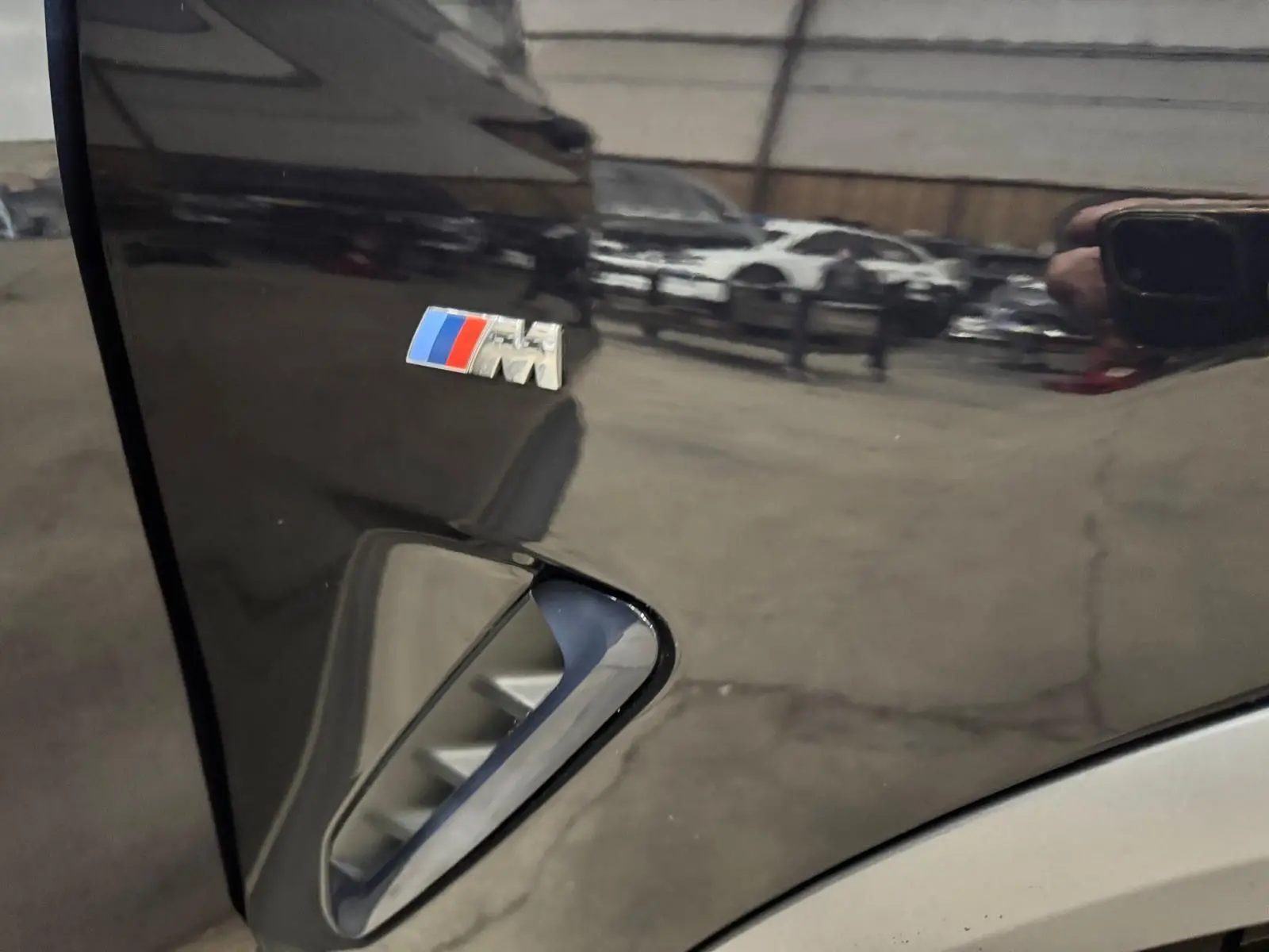 Gros plan sur l'aile avant gauche noire d'une BMW X4 M SPORT avec logo M coloré et prise d'air latérale.