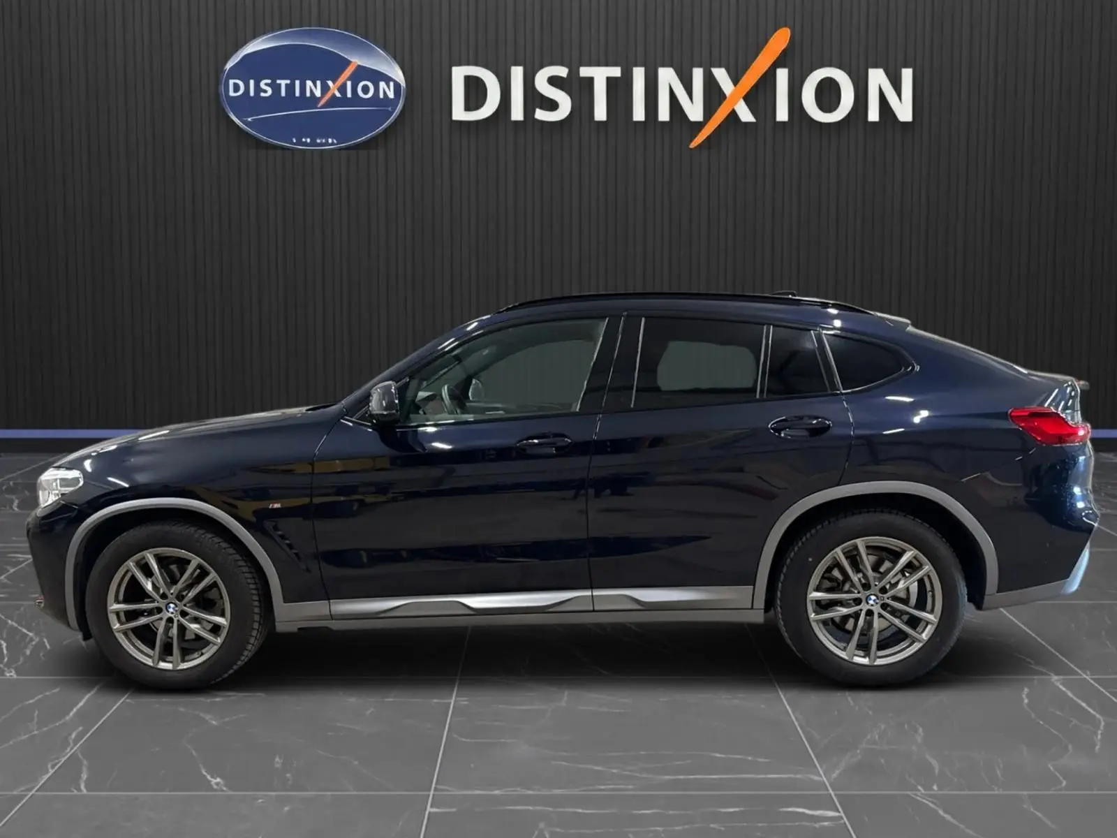 BMW X4 XDrive 20d M SPORT 2020 en carbonschwarz, vue profil côté gauche sur fond intérieur noir avec logo Distinxion.