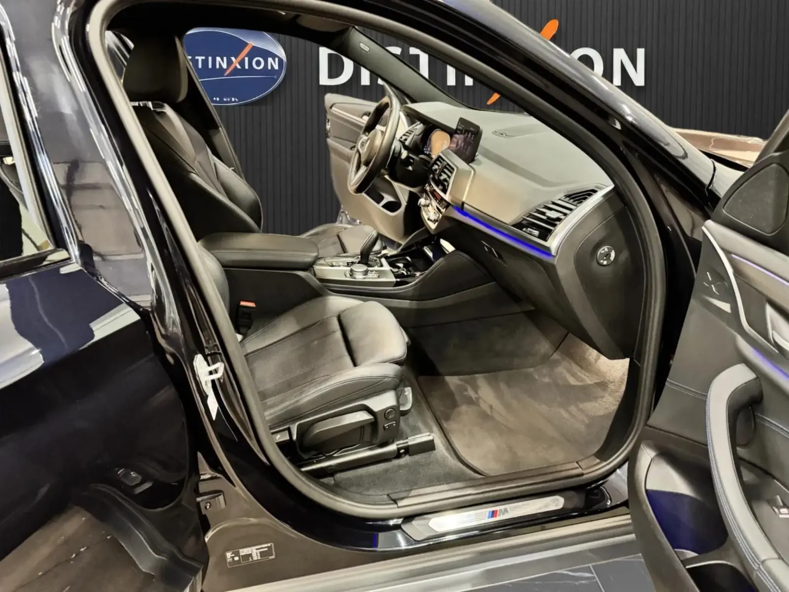 Vue intérieure côté conducteur de la BMW X4 XDrive 20d 2020 en Carbonschwarz, avec sièges cuir noir et éclairage d'ambiance bleu.
