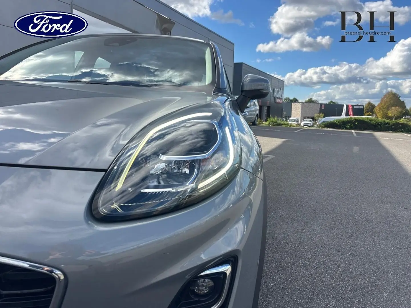 Gros plan sur le phare avant droit du Ford Puma gris Solar métallisé sous un ciel partiellement nuageux.
