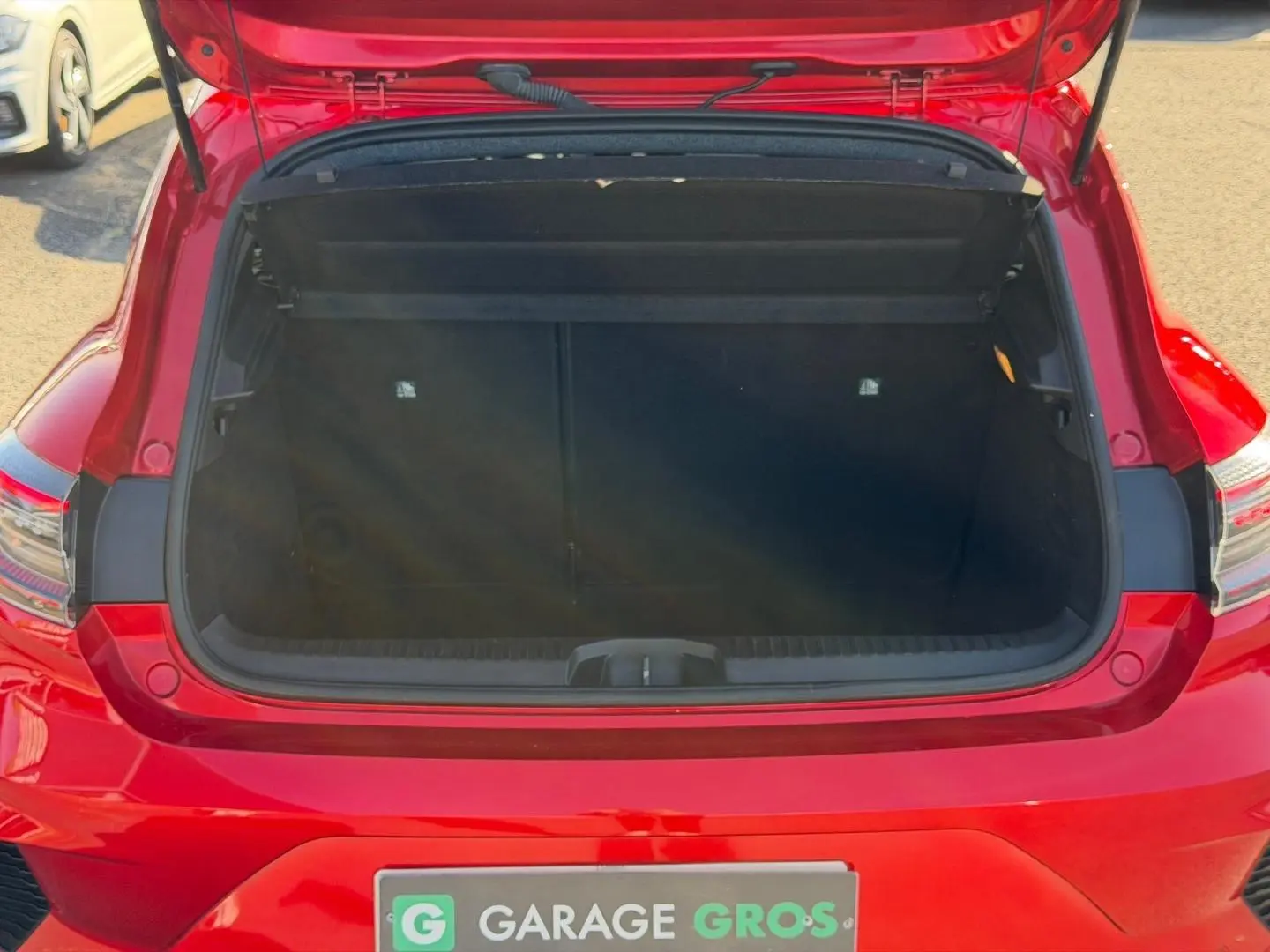 Coffre ouvert vu de l'arrière d'une Renault Clio rouge, montrant l'espace de chargement vide.