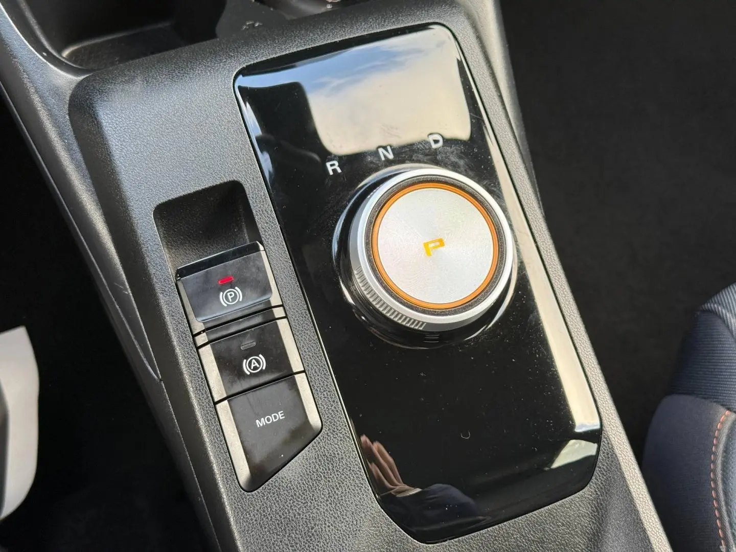 Gros plan sur la console centrale noire du MG3 blanc 2025, avec sélecteur rotatif de boîte auto et boutons de frein à main électronique.