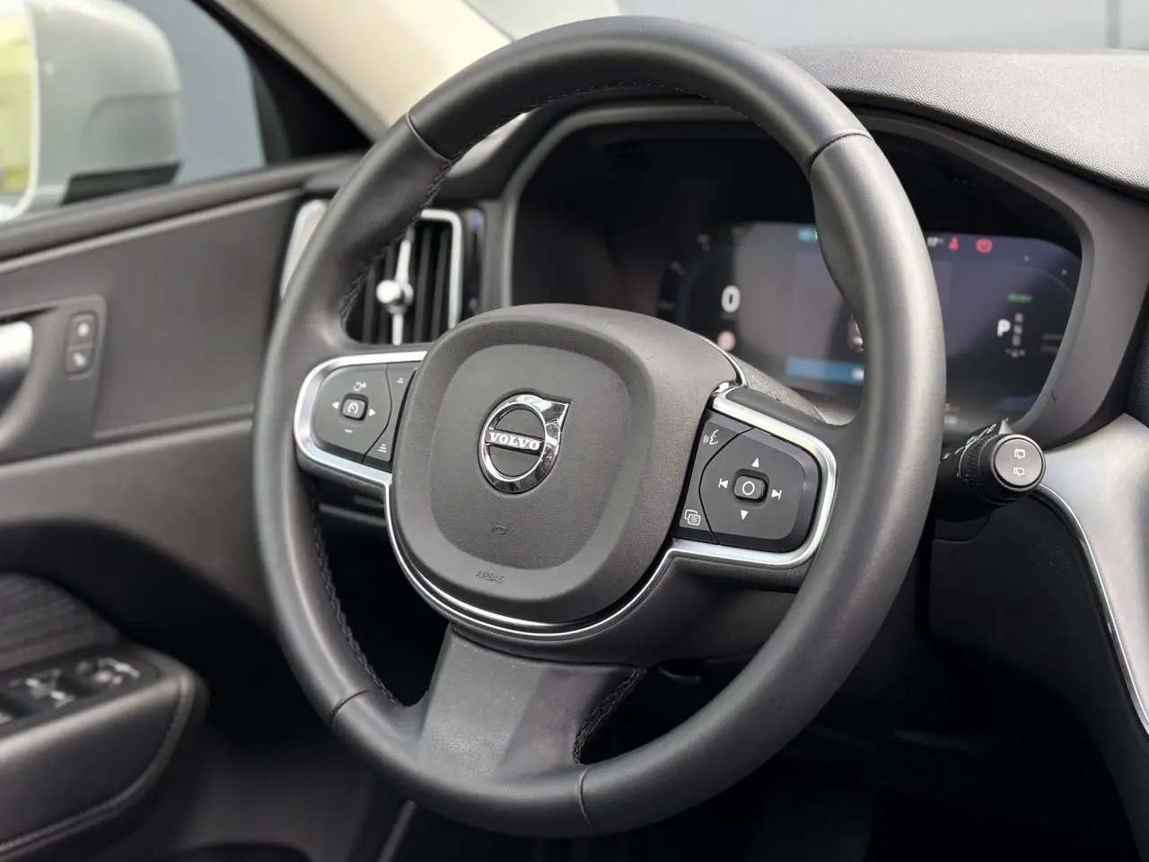 Volant simili-cuir noir de Volvo XC60 T6 AWD PHEV 2024 vu de face avec commandes intégrées et tableau de bord digital.