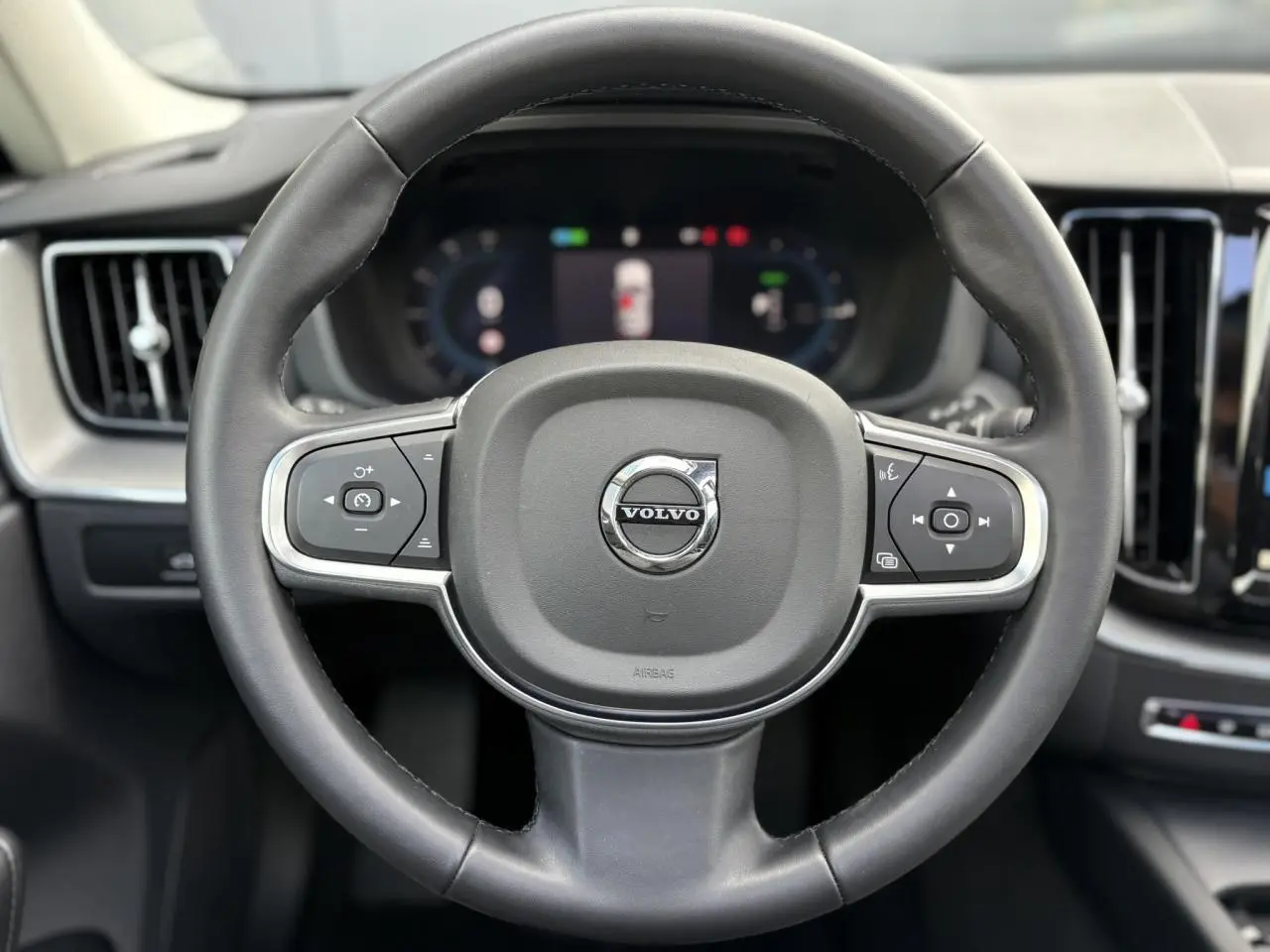 Volant simili-cuir noir de Volvo XC60 2024 avec commandes intégrées et tableau de bord digital en arrière-plan.