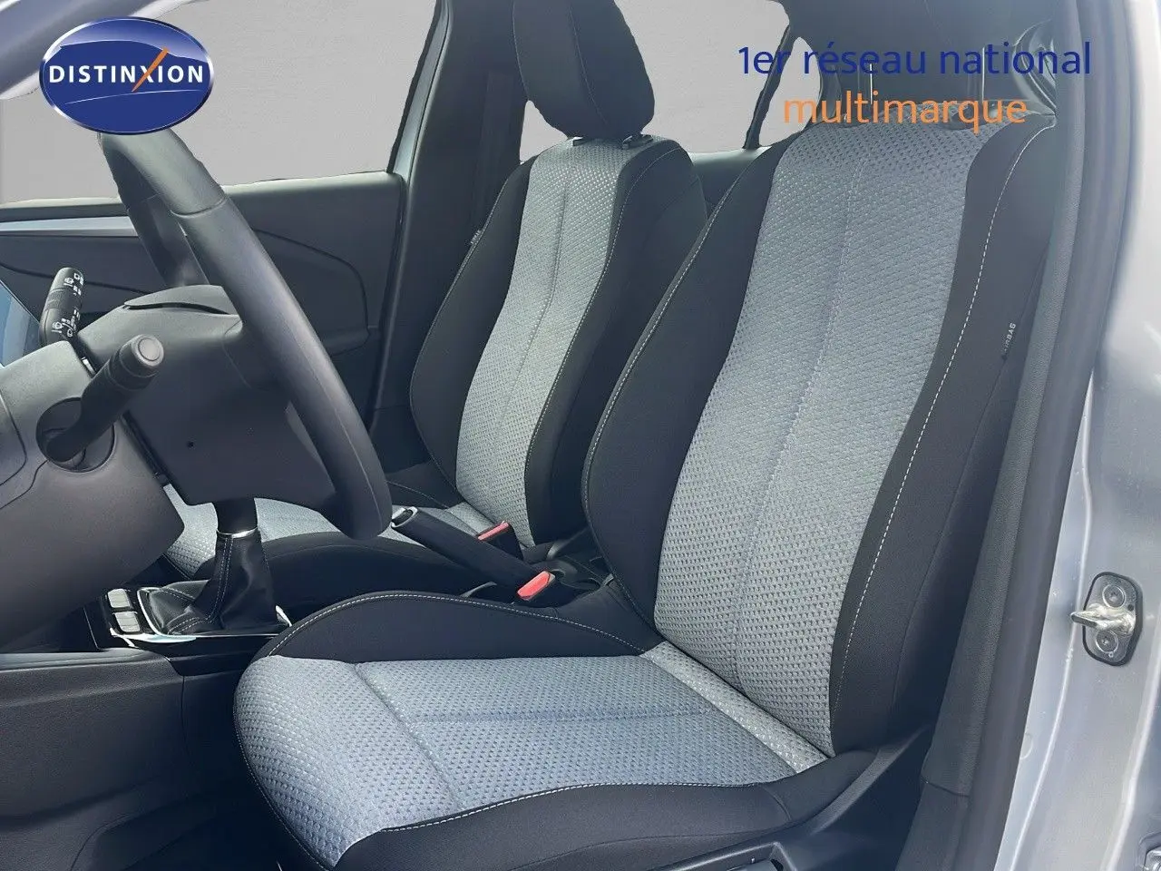 Vue intérieure côté conducteur de l'Opel Corsa 2025 avec sièges tissu gris clair et noir, volant et levier de vitesse manuelle visibles.