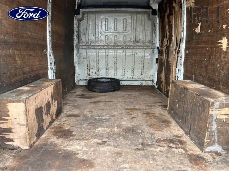 Vue intérieure arrière du fourgon Citroën Jumper blanc, montrant l'espace de chargement usé avec une roue de secours posée au fond.