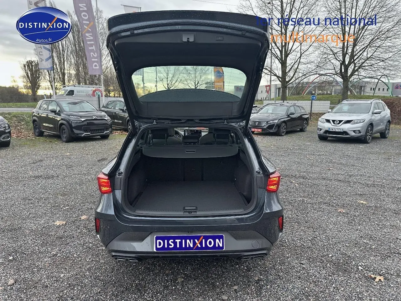 Vue arrière d'une CUPRA LEON ST gris magnétique avec coffre ouvert, feux arrière LED allumés, sur parking extérieur.