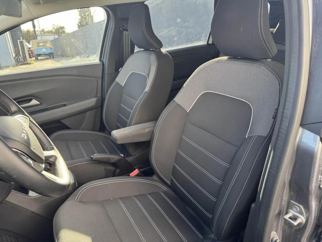 Vue intérieure côté conducteur du Dacia Jogger gris schiste, mettant en valeur les sièges avant en tissu noir avec surpiqûres blanches.