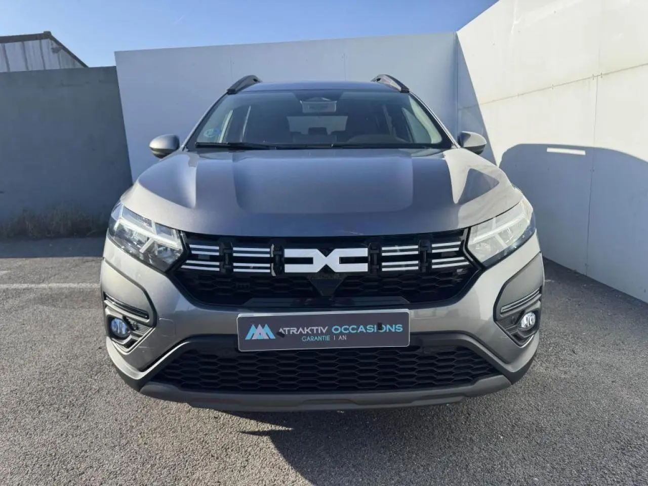 Vue frontale d'un Dacia Jogger gris schiste métallisé avec calandre noire et feux LED allumés.