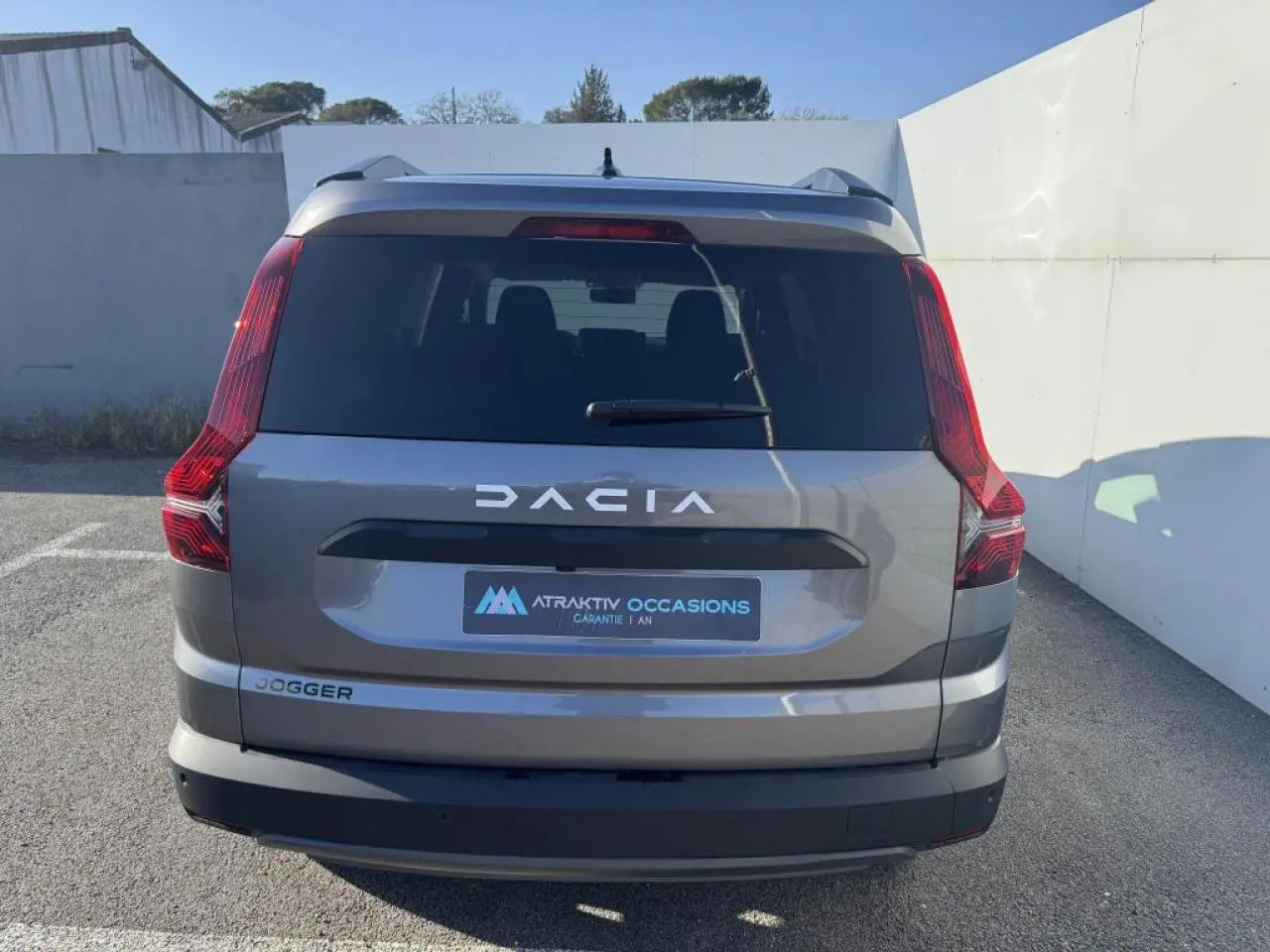 Vue arrière d'un Dacia Jogger gris schiste métal avec feux arrière verticaux et logo DACIA visible.