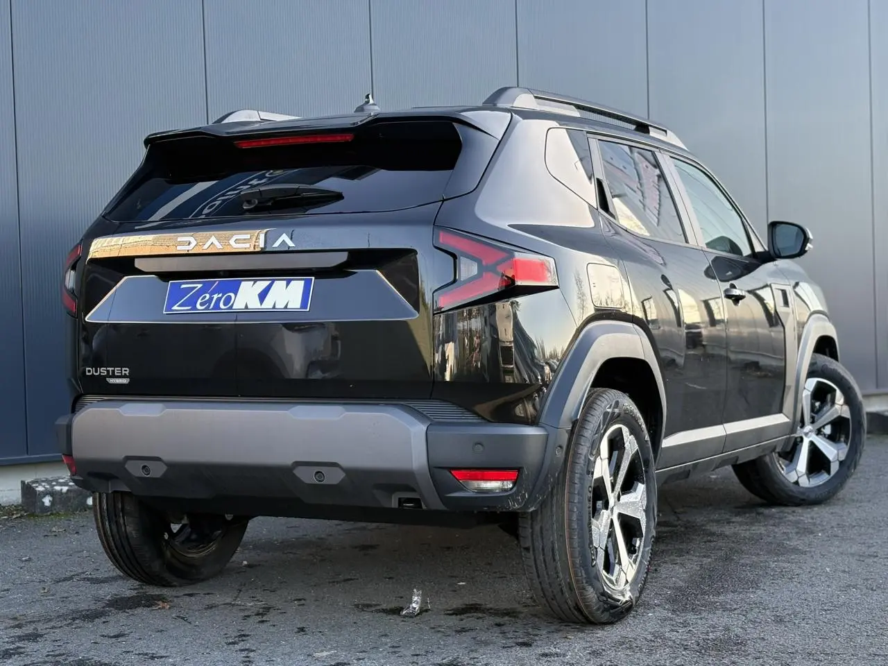 Vue 3/4 arrière droite du Dacia Duster 2025 noir nacré avec jantes alliage et barres de toit longitudinales.