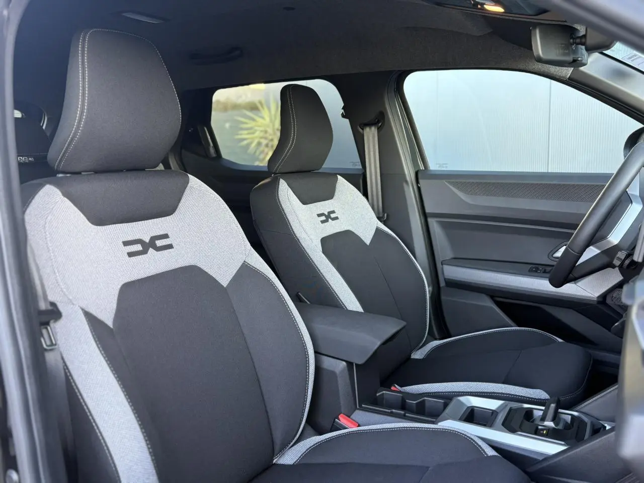 Vue intérieure côté droit du Dacia Duster 2025, sièges bi-ton gris et noir avec logo DC brodé.