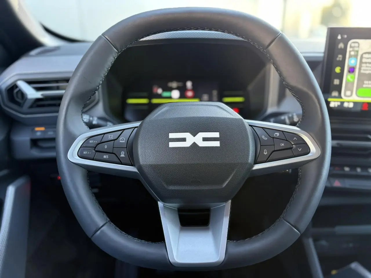 Vue frontale du volant noir du Dacia Duster 2025 avec commandes intégrées et tableau de bord digital en arrière-plan.