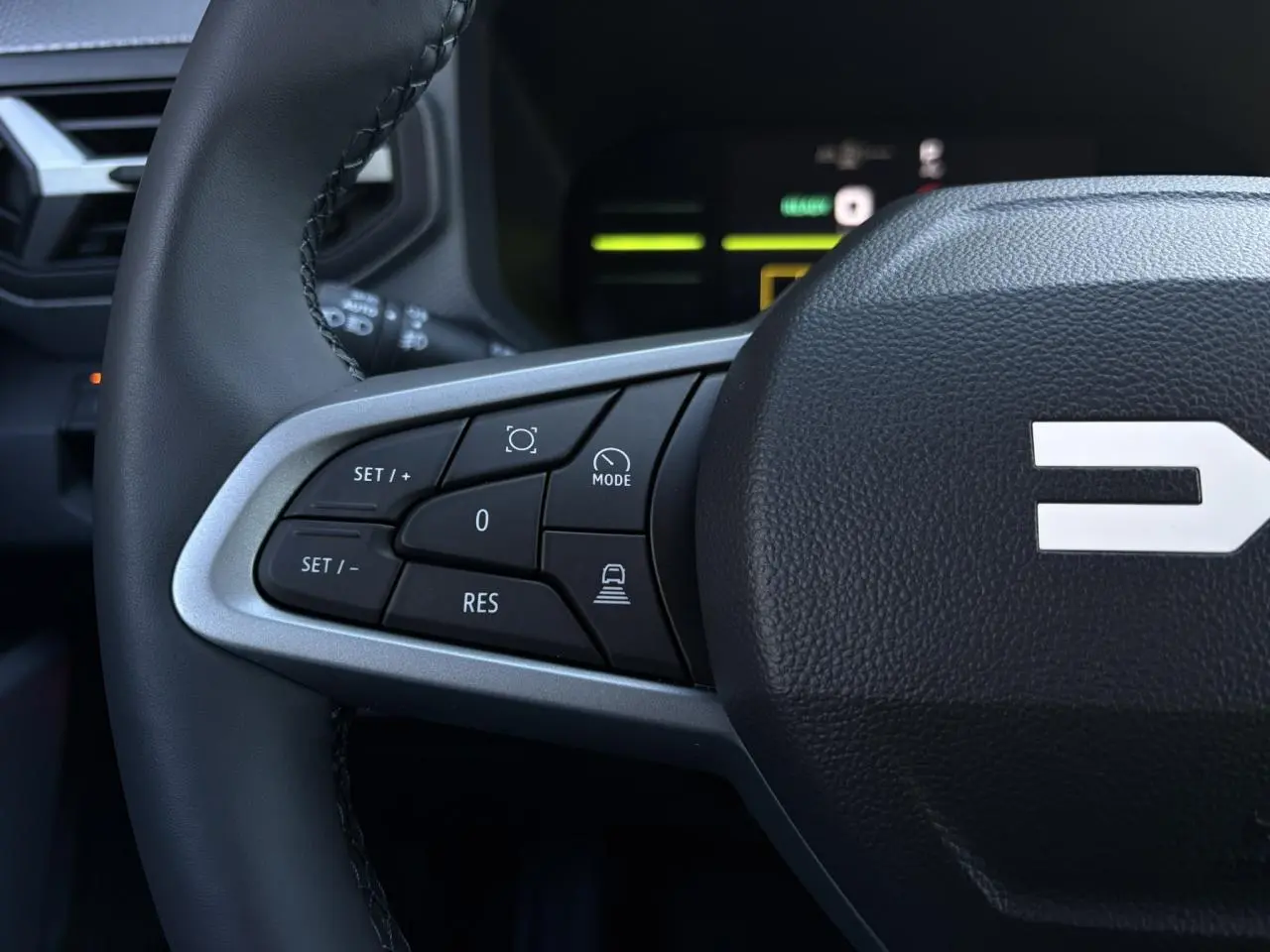 Gros plan sur le côté gauche du volant noir du Dacia Duster 2025 avec commandes de régulateur et assistance.