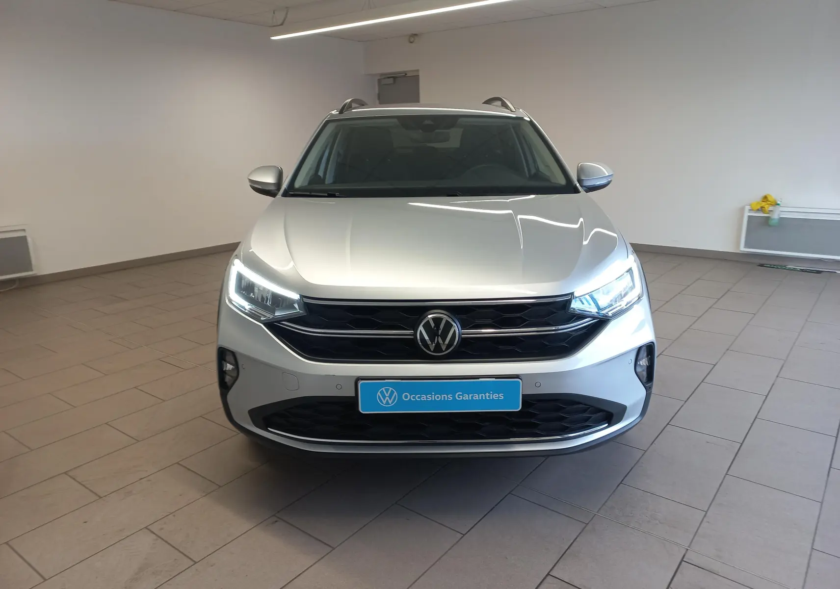 Vue avant d'un Volkswagen Taigo 2025 argent métallisé avec phares LED allumés et calandre noire brillante.