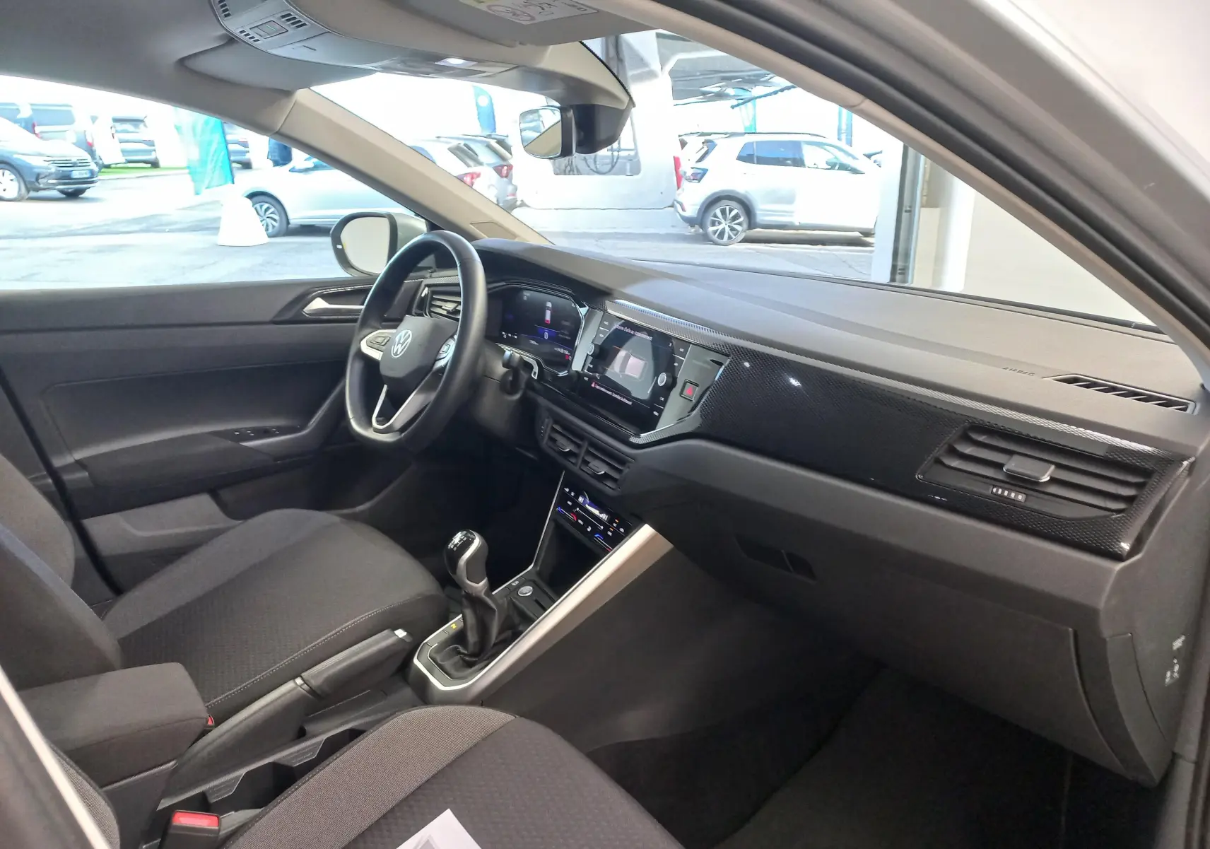 Vue intérieure côté conducteur du Volkswagen Taigo 2025, tableau de bord noir avec volant multifonction et levier de vitesses manuel.