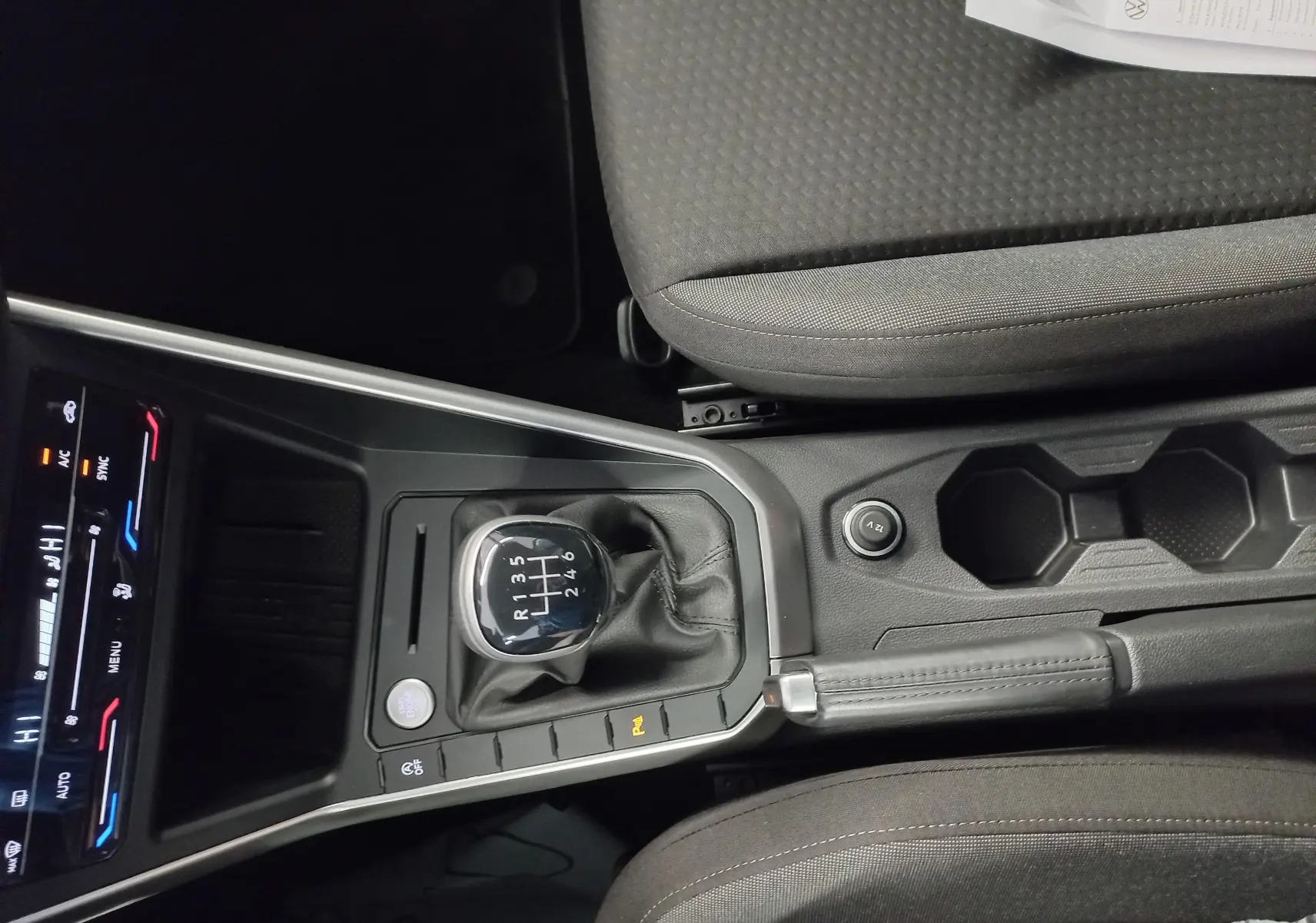 Vue intérieure centrée sur la console centrale du Volkswagen Taigo 2025, avec levier de vitesse manuel et sièges gris.