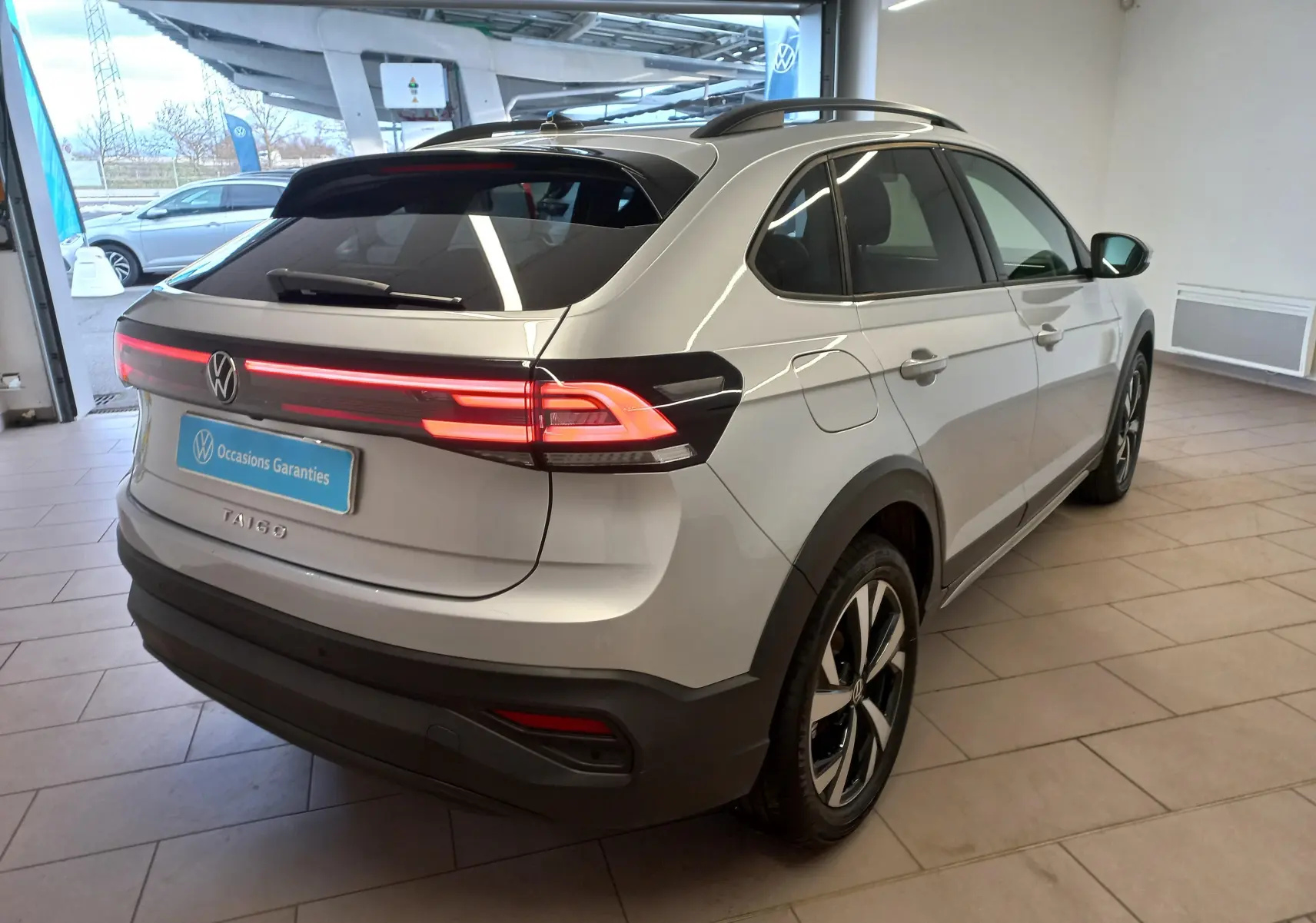 Volkswagen Taigo 2025 en reflet d'argent, vue 3/4 arrière droit, feux arrière LED allumés et jantes alliage 17 pouces.