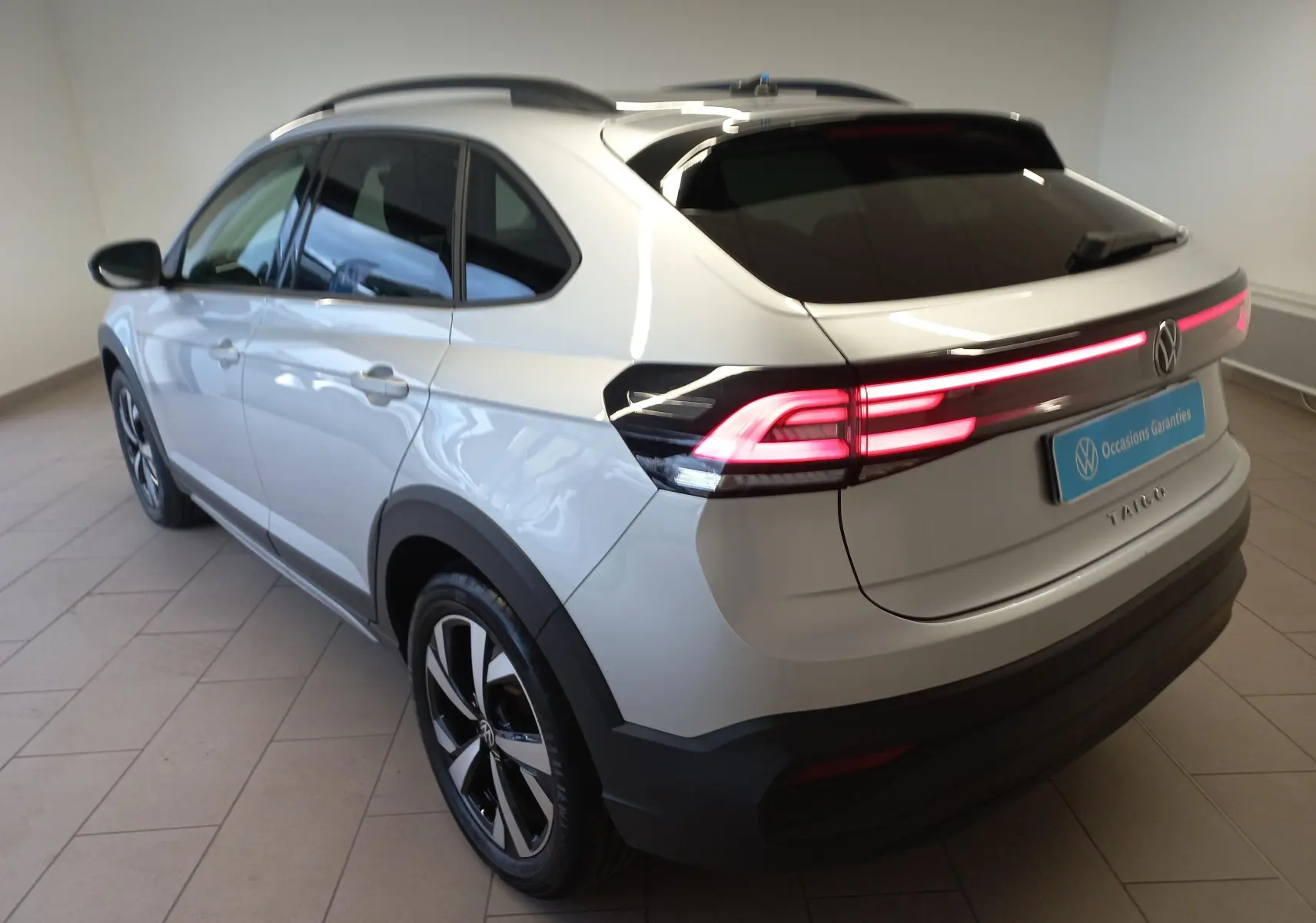 Volkswagen Taigo argent métallisé vue 3/4 arrière droit avec feux arrière LED allumés et jantes alliage 17 pouces.