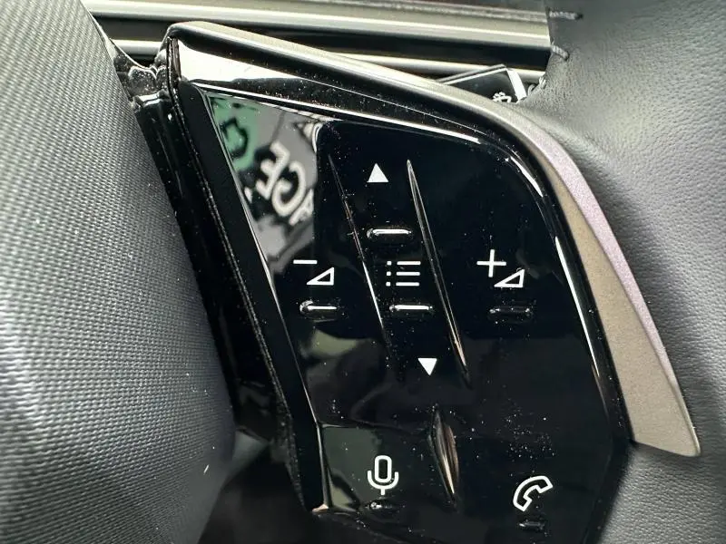 Gros plan sur les commandes au volant noir brillant du Peugeot 3008 Hybrid 2025, avec icônes blanches pour audio et appel.