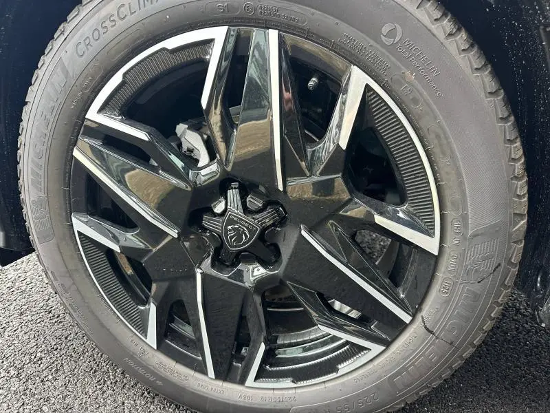 Gros plan sur la jante alu noire et argentée du côté gauche d’un Peugeot 3008 bleu 2025 hybride.